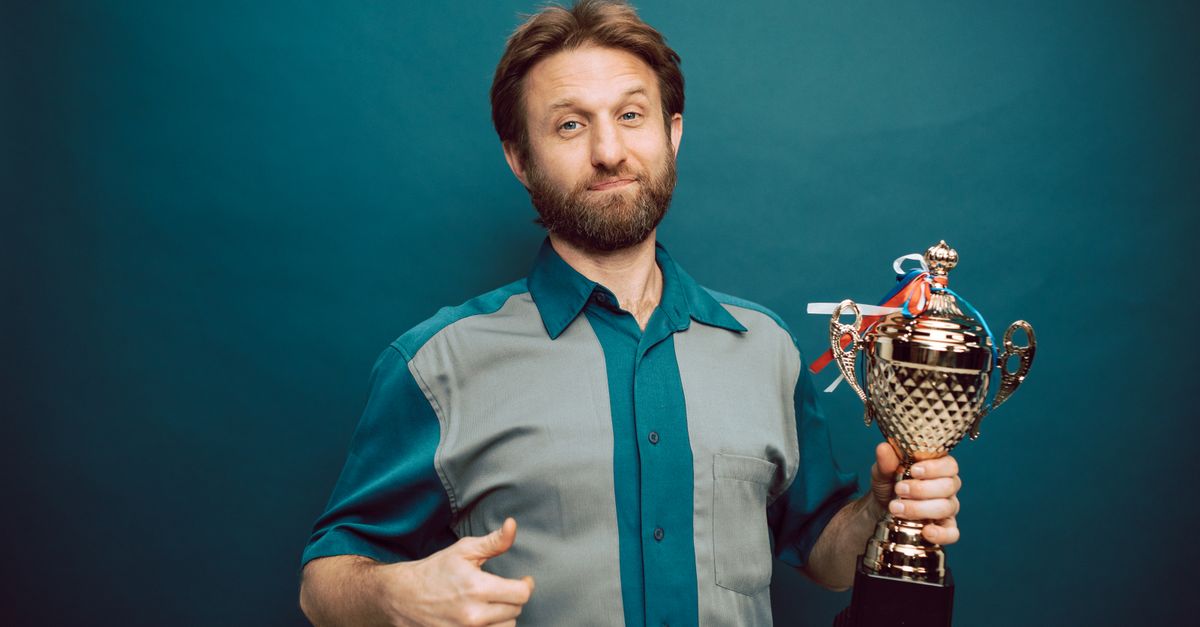 Confident man posing in studio holding a shiny trophy, showing pride in accomplishment.